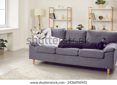 Tired half man half animal enjoying well deserved rest at weekend. Funny relaxed man in rabbit face mask, white shirt, trousers and glasses sleeping with hands behind head on comfortable sofa at home Royalty-Free Stock Photo #2436096943