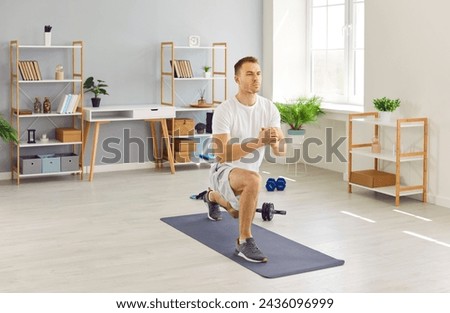Focused young man in activewear having a fitness workout at home, standing on a yoga mat in the living room, and doing a forward lunge exercise. Sport, wellness, physical activity concept