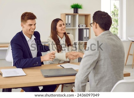 Happy couple signing a contract and shaking hands with business broker man or insurance agent. Young man and woman having a good deal with their investment adviser sitting in the office.