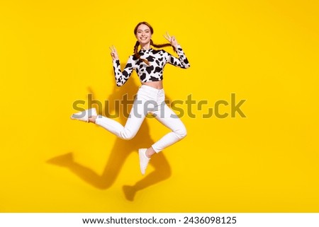 Full size portrait of carefree pretty girl jump demonstrate v-sign empty space isolated on yellow color background