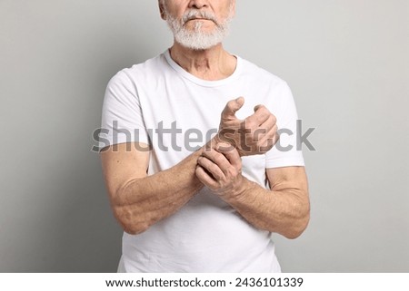 Arthritis symptoms. Man suffering from pain in wrist on gray background, closeup Royalty-Free Stock Photo #2436101339