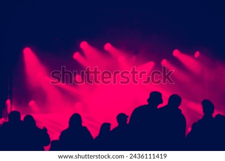 Silhouette of cheering crowd at a concert. Colorful bright stage lights in the background