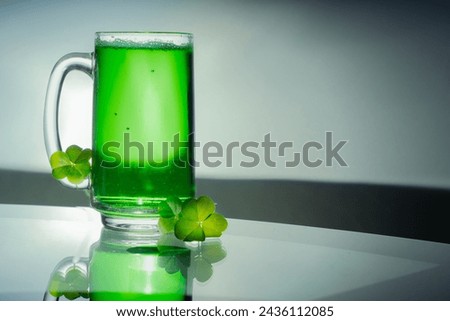 Green drink in a clair glass next to clovers on a glass table with copy space to the right.