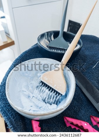 Rich, creamy hair dye mix rests on a wooden brush over a sleek bowl. The tools for hair coloring lie on a dark, textured towel, with a hint of vibrant pink peeking through, suggesting the lively work Royalty-Free Stock Photo #2436112687