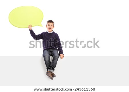 Male kid holding a speech bubble seated on panel isolated on white background