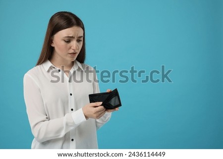 Sad woman showing empty wallet on light blue background, space for text