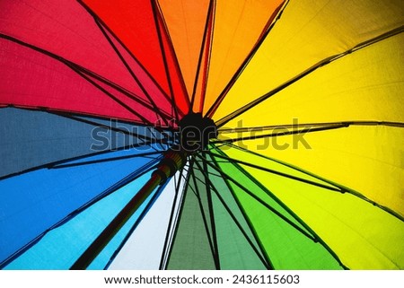 A rainbow umbrella with a black handle. The umbrella is open and the colors are vibrant. Concept of joy and happiness, as the rainbow colors are often associated with positivity and good luck