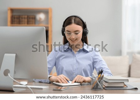 E-learning. Young woman taking notes during online lesson at table indoors