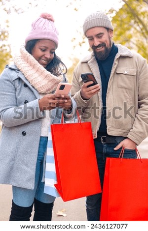 Smiling young multiracial couple holding shopping bags, browsing smartphone apps.Vertical