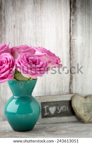Pink roses in a vase with a Valentine's Day decoration on a wooden shelf.