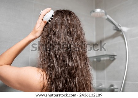 Young woman with dark curly hair doing self hair scalp massage with scalp massager or hair brush for hair growth stimulating at home bathroom. High quality photo