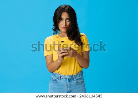 Woman with a phone in her hands with a yellow case on a blue background in a yellow T-shirt, emotions signals gestures, online lifestyle concept, shopping, communication, learning, business online