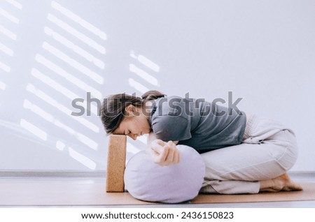 Woman in casual clothing doing yin yoga crossed arm stretch with bolster and cork block Royalty-Free Stock Photo #2436150823