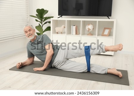 Senior man doing exercise with fitness elastic band on mat at home Royalty-Free Stock Photo #2436156309