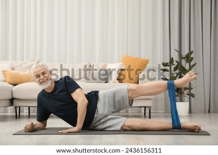 Senior man doing exercise with fitness elastic band on mat at home Royalty-Free Stock Photo #2436156311