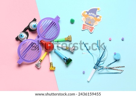 Funny glasses with party whistles and decor on color background. April Fools Day prank