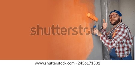 Handsome young painter man with happy smile and class gesture painting the wall. Repair, building and home concept. Banner. Copy space