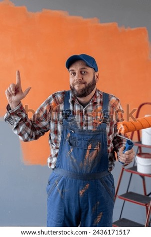 Painter caucasian man showing and lifting a finger in sign, standing on wall background. Copy space