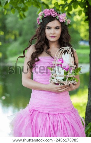 Cute fashion model woman with healthy hair and natural makeup wearing pink dress against green summer background outdoor