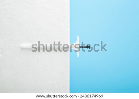 New white plastic insulation anchor dowel and styrofoam panel on blue table background. Pastel color. Closeup. Material for house thermal protection. Home facade repair work preparation. Top view.