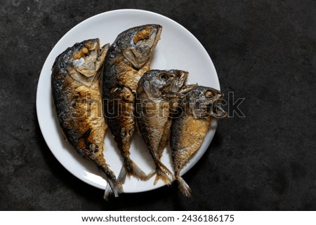 Top view. Image of fried mackerel on a white plate placed on the kitchen floor in a home