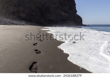 Wave washing over Foot prints in black volcanic sand on empty beach in Gran Canaria, Spain. Image 3 of 5
