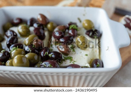 Oven baked feta cheese with marinated black and green  olives in a casserole dish