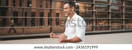 Emotional smiling Mature businessman with neat beard wearing white shirt is walking on the street of modern city, Panorama. Successful man relaxed, enjoying life