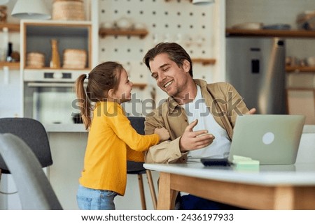 A little girl wants her dad to play with her while he's working from home, online. Royalty-Free Stock Photo #2436197933