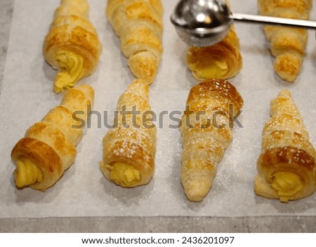 View with depth of field of custard cream filled horns or cone being topped with powdered sugar with a dusting wand.