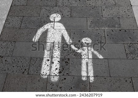 Pedestrian crossing sign consisting of two white figures, an adult and a child holding hands. Safe area for pedestrians on sidewalk