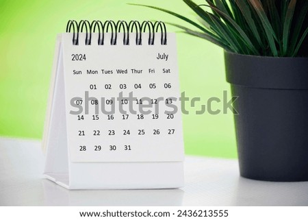 July 2024 desk calendar with potted plant on a desk with green background.
