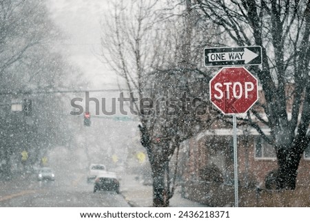 Snow falling in winter on street with stop sign and trees cars driving