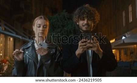 Couple walking city outside street night European woman and Indian Latino Arabian man texting using smartphone mobile phone multiracial disorder problem frustrated offended girl ignore guy separation Royalty-Free Stock Photo #2436219505