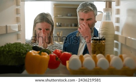 POV Point of view from inside fridge adult couple feeling bad disgusting unpleasant smell from broken refrigerator spoiled rotten food meal middle-aged man and woman awful smelling stink from freezer Royalty-Free Stock Photo #2436219581