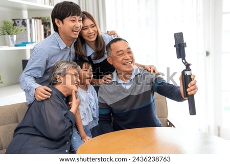 Big family, including a grandfather, are taking a selfie with a cell phone. The grandfather is holding the phone and smiling, while the other family members are gathered around him