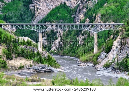 Long  train bridge extends over river in the remote mountain area of Alaska. Royalty-Free Stock Photo #2436239183