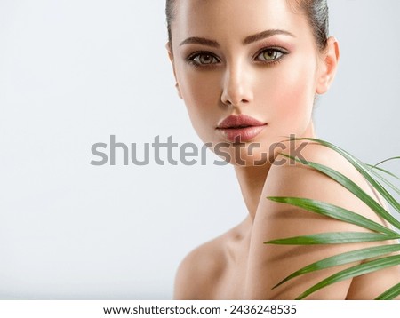 Young beautiful woman with healthy skin of face and palm leaves. Closeup fresh face of an attractive caucasian girl with green plants. Model with bright brown eye makeup. Skin care concept.  Royalty-Free Stock Photo #2436248535