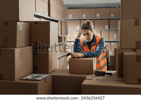 Exhausted sad warehouse worker having a break, she is leaning on a pile of boxes and touching her head