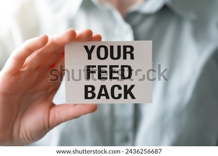 Close-up of businesswoman in white shirt holding a card with Your Feedback text in modern office interior. Employee giving positive feedback to company. Business concept. High quality photo