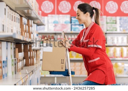Female stock clerk working at the supermarket, she is standing on a ladder and smiling