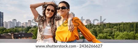 appealing jolly women in vibrant clothes with sunglasses smiling at camera while on roof, banner