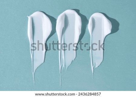 Three strokes of white cream on a blue background. Royalty-Free Stock Photo #2436284857