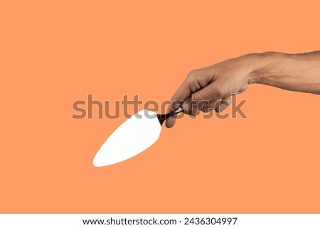 Black male hand holding a cake cutter knife isolated on orange background Royalty-Free Stock Photo #2436304997