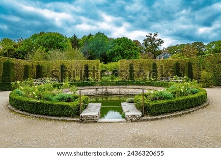 Picturesque round pool in the park greenhouse. The“possession of Puss in Boots”. Graceful bosquets surround the pool in Breteuil Park. Castle of Breteuil. France Royalty-Free Stock Photo #2436320655