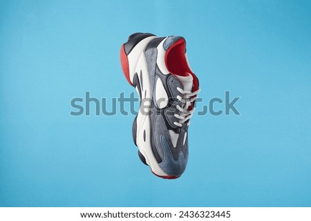 Stylish sports sneaker with stout sole levitating on a blue background. Creative minimalistic footwear concept. Fashion shoes in the air.