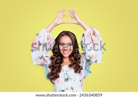 Portrait of good-looking, magnificent, exquisite brunette showing love symbol, heart shape with fingers above head looking at camera isolated on bright teal background