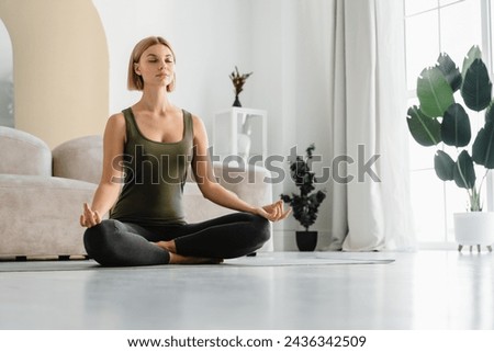 Relaxed young woman doing sitting in yoga position at home. Female athlete sitting in lotus meditating. Serene people concept. Life balance Royalty-Free Stock Photo #2436342509