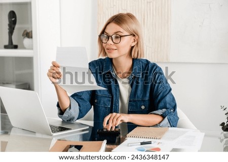 Young caucasian woman paying domestic bills, making calculations at home desk. Female holding billing overdue, counting funds online, loan and debt Royalty-Free Stock Photo #2436348147
