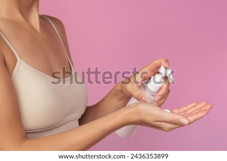 A young woman in beige underwear applies a moisturizer from a bottle to her hand using a dispenser. Body care. Moisturizing and nourishing the skin. Isolated on a pink background. Profile photo